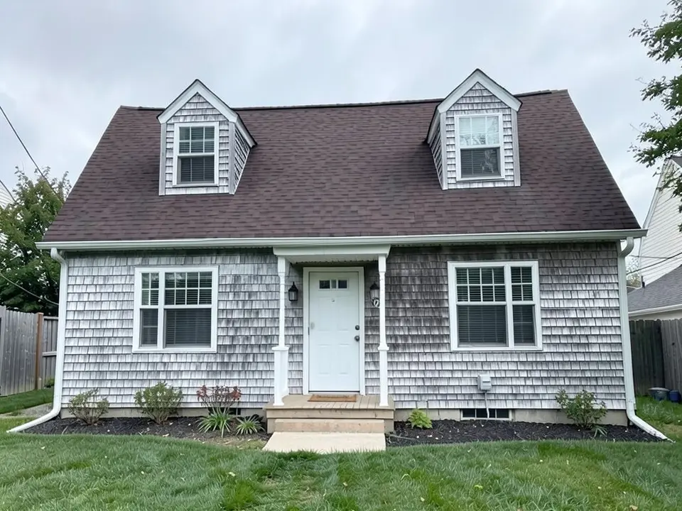 The same house with silver-gray weathered cedar shakes on the walls and both dormers; white trim, white door and brown roof kept