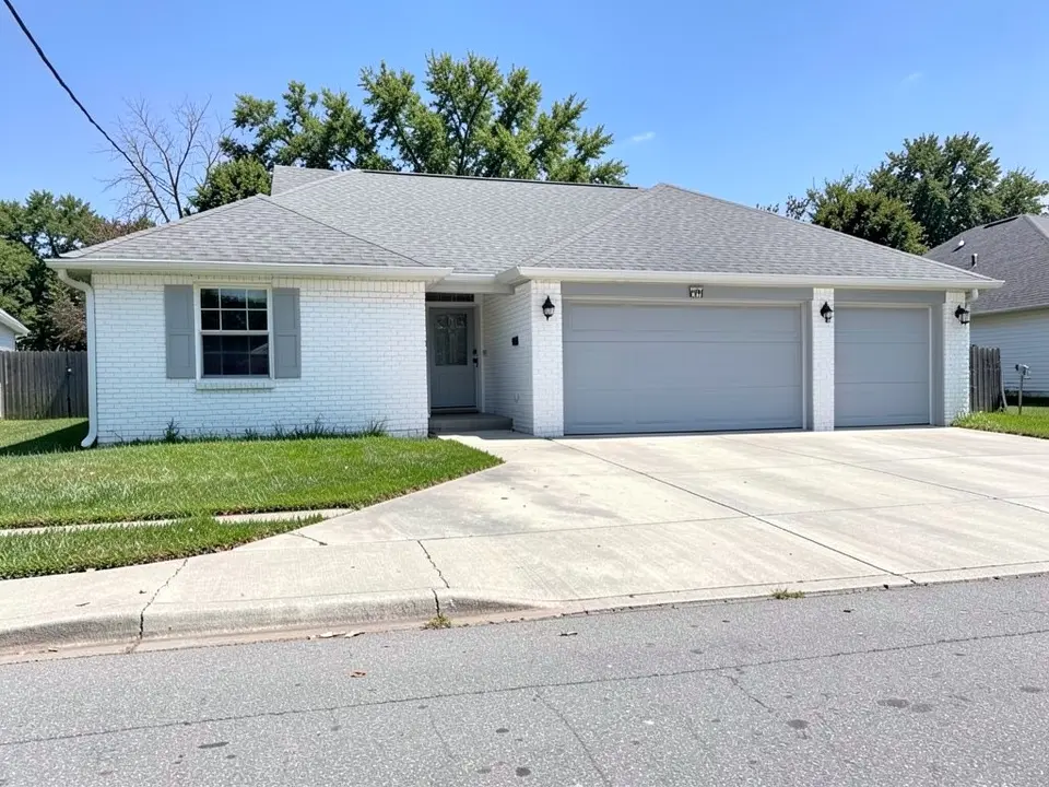 Single-story ranch house with white painted brick, gray shutters and gray garage doors