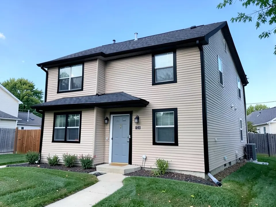 The same house with black window frames on the front wall, black fascia, gutters and outer corner boards; beige siding, gray front door and roof kept