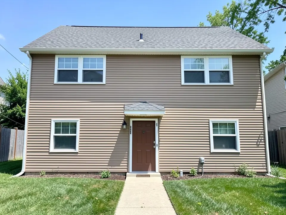 AI-drawn stand-in of a plain two-story house seen straight on, with tan vinyl lap siding, a gray shingle roof, two double windows upstairs and two windows downstairs with narrow white trim, and a brown front door under a small hood