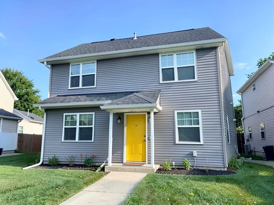 The same house with a bright yellow front door; siding, trim, porch and roof kept