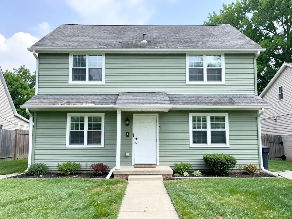 AI-drawn generic stand-in of a two-story sage green vinyl-sided house with white trim, a white front door and a weathered, stained gray asphalt shingle roof over the main house and the porch