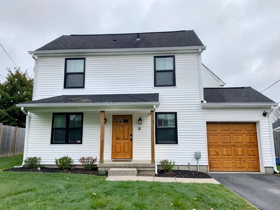 The same house with a warm wood-colored front door and garage door; the white siding, black window frames, porch posts, roof and lawn kept