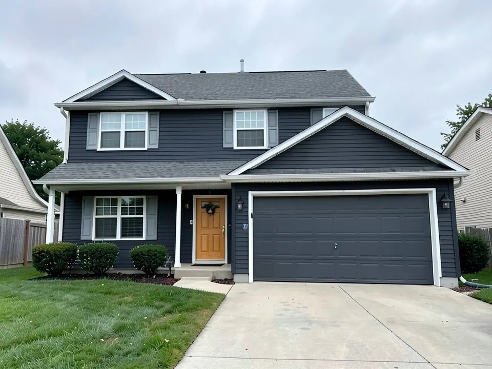 The same house with deep charcoal siding on every wall, a honey-toned wood front door with the wreath still on it, a dark gray garage door, gray shutters and white trim