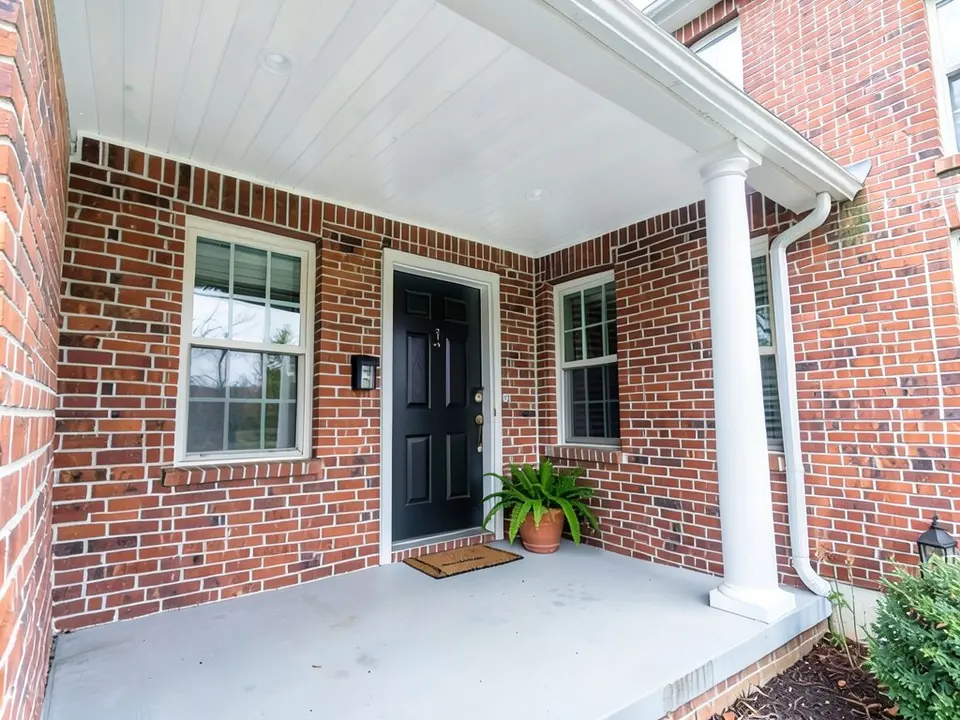 The same porch with a soft white ceiling; brick, column, floor, door and fern kept
