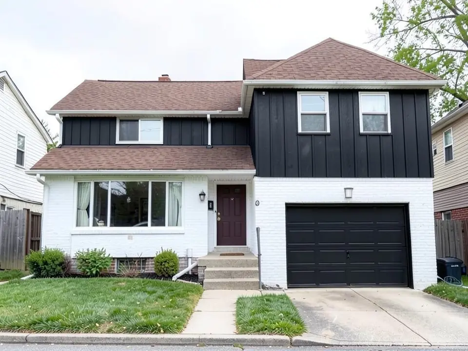 The same split-level with the brick painted white, black vertical board and batten siding on the upper floor and a black garage door; the brown front door, roofs and windows unchanged