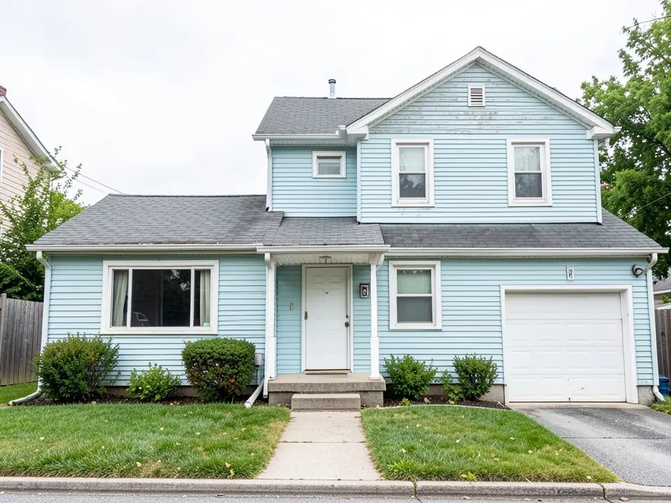 Two-story house with a one-story wing, in pastel light blue horizontal siding with white trim, a gray shingle roof and a white one-car garage door