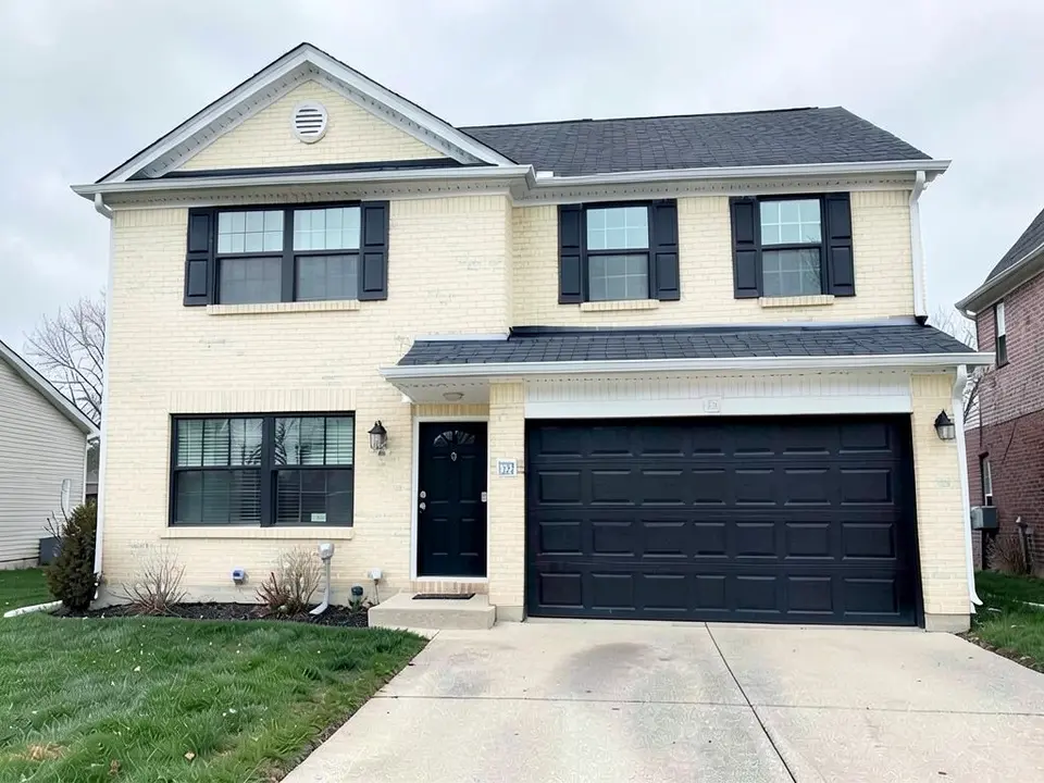 The same house with all the brick painted a pale cream-yellow, with the brick joints still visible; the black shutters, door, garage door and roof kept